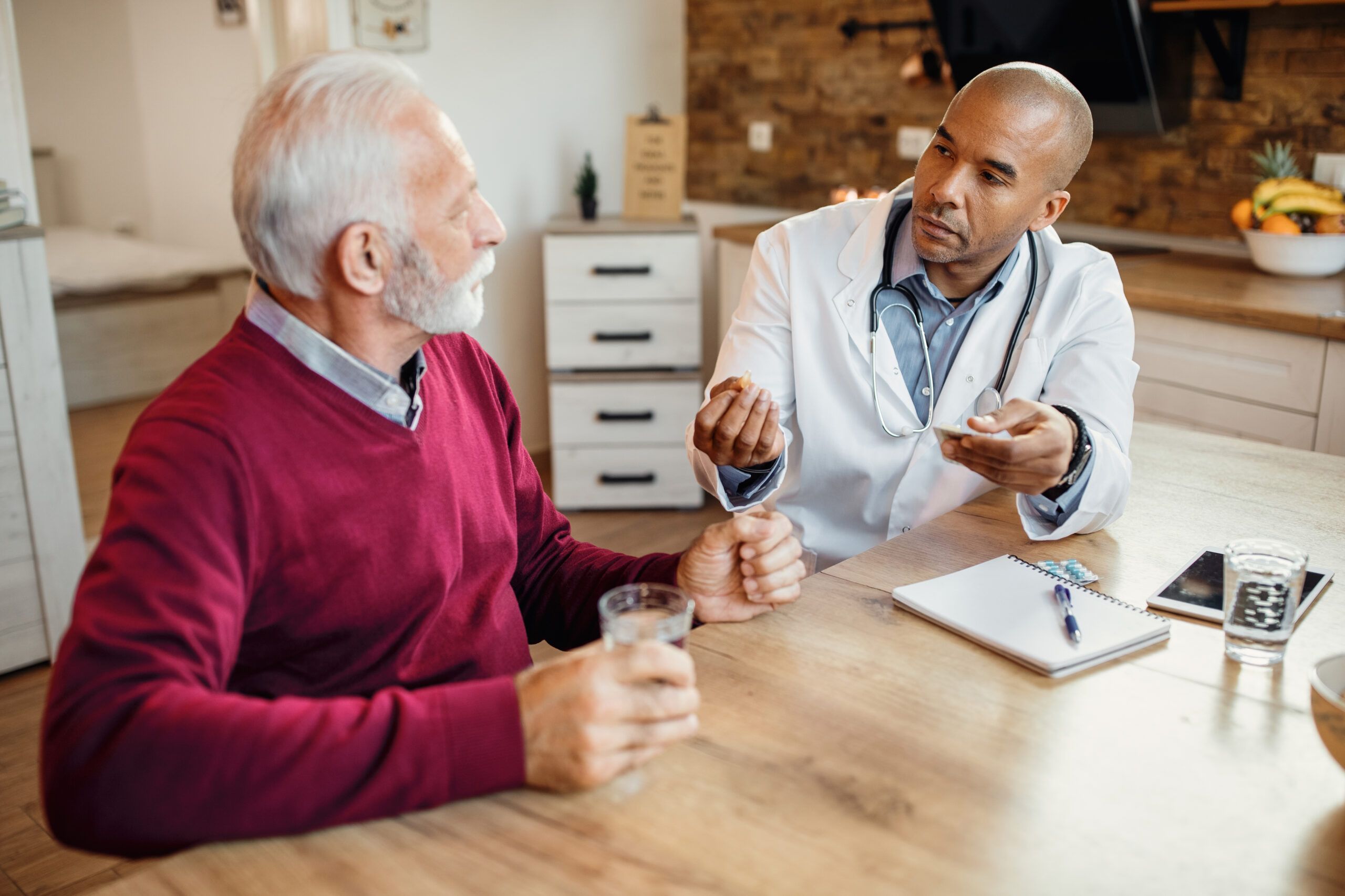 African American doctor visiting senior man at home and giving his a medicine.